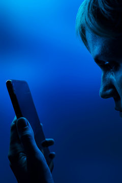 Young woman is looking into smartphone. Neon classic blue light, vertical photo. Part of woman&rsquo;s face is visible in profile. Copyspace. Concept of technology, future, social networks, content, mobile.