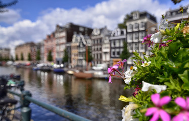 Fototapeta na wymiar Amsterdam,Holland,August 2019. Enchanting view of a canals of the historic center. The typical houses overlook the water, boats moored along the canal. Planters on railings and bikes. Sunny day.