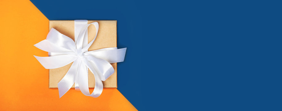 Banner with trendy attractive minimalistic gift on the orange and blue background. Merry Christmas, St. Valentine's Day, Happy Birthday and other holidays concept.