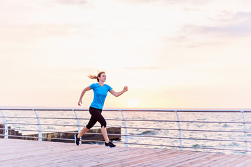 Attractive woman in blue shirt running along seashore at sunrise