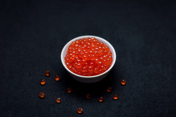 Red Caviar in a spoon. Caviar in bowl over black background. Close-up salmon caviar. Seafood. Delicatessen. Gourmet food. Texture of caviar. 