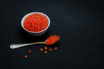 Red Caviar in a spoon. Caviar in bowl over black background. Close-up salmon caviar. Seafood. Delicatessen. Gourmet food. Texture of caviar. 