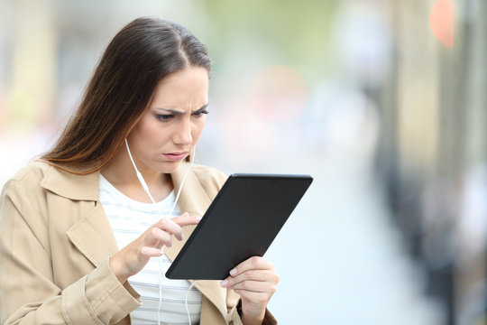 Frustrated girl with earphones checking media on tablet