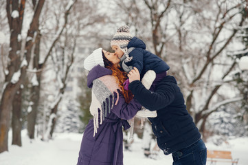 Family have fun in a winter park. Stylish mother in a purple jacket. Little girl in a winter clothes. Father with cute daughter