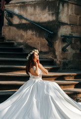 Bride in luxury wedding dress sits on the stone stairs