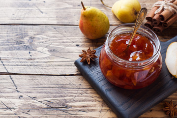 Homemade pear jam in a jar and fresh pears on a wooden background. Copy space.