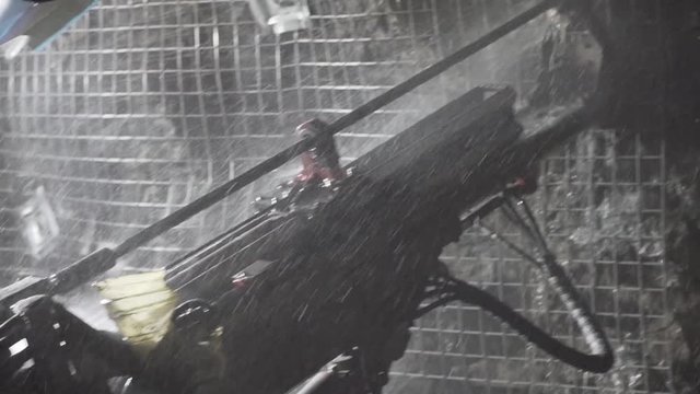 Reveal of underground jumbo drilling into hard rock with water spurting out to hold up mesh