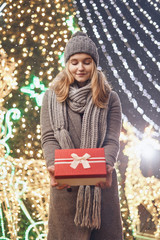 Girl holding gift box on winter festival. Happy woman with Christmas gift over Christmas background.