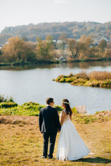 Amazing newlyweds go to the lake holding hands on a sunny day