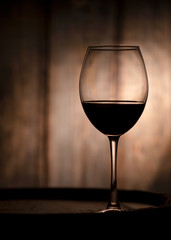 Glass with red wine and a wooden barrel close-up. Glass of wine on a wooden background.