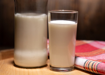 Bottle of milk, a glass and a checkered napkin. Rustic milk on a wooden background. Still life with rustic milk.