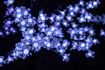Luminous garland of decorative flowers on a tree. Christmas tree decorated with bright bulbs