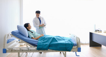 Asian Male doctor is talking to female patients lie in bed in the hospital room about the diagnosis...