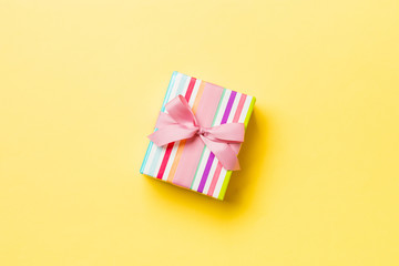 wrapped Christmas or other holiday handmade present in paper with pink ribbon on yellow background. Present box, decoration of gift on colored table, top view with copy space