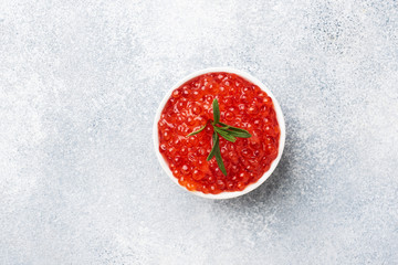 Red salmon caviar in a plate on Gray concrete background. Snack delicacy. Copy space.