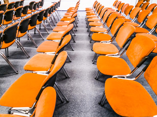Meeting room interior. Front view of rows of orange chairs standing in an auditorium. Seats in an...
