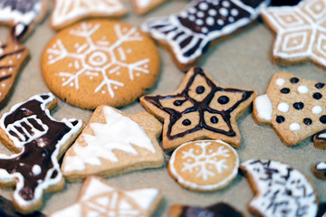 Many different shapes and drawings of homemade Christmas gingerbread on paper. The cookies are decorated with white glaze and chocolate. Close up view with bokeh