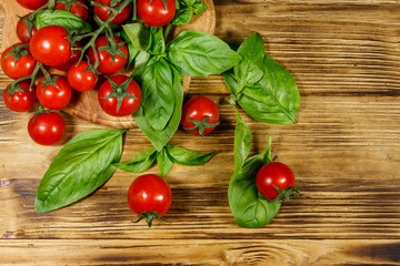 Fresh cherry tomatoes with green basil leaves on a wooden table. Top view