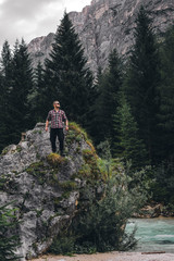 Obraz premium Man on a large stone, a boulder, among the incredibly beautiful river of turquoise color, vertical photo. Dolomites mountains, Camping Olympia Fiames, Cortina Ampezzo Italy.