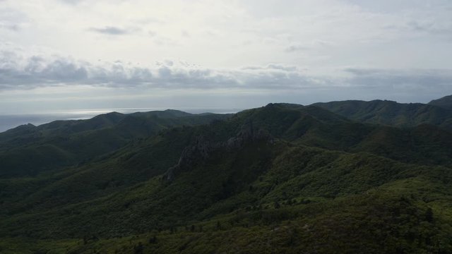 Epic open shot of a huge megalithic formations on top of a forested mountain ridge with ocean in the far distance on a cloudy day. Aerial shot.