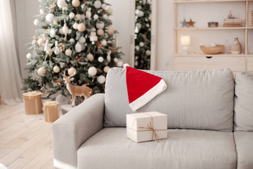 Christmas gift craft box on the sofa .Christmas tree background in home interior. Red hat Santa behind