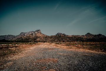Country road in the mountains . A wide empty road in the desert toward distant mountains . gravel and dirt, sunny summer day . car road Gravel Road in mountains  as the background  in Thailand