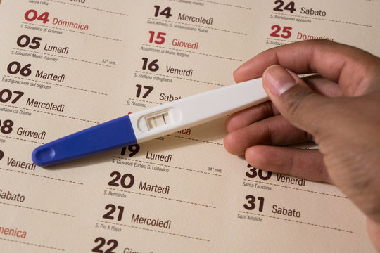 Woman holding a positive pregnancy test on a wooden desk