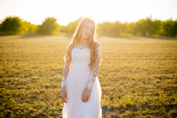 Fototapeta na wymiar Young woman is in her bridal dress and smiling in field.