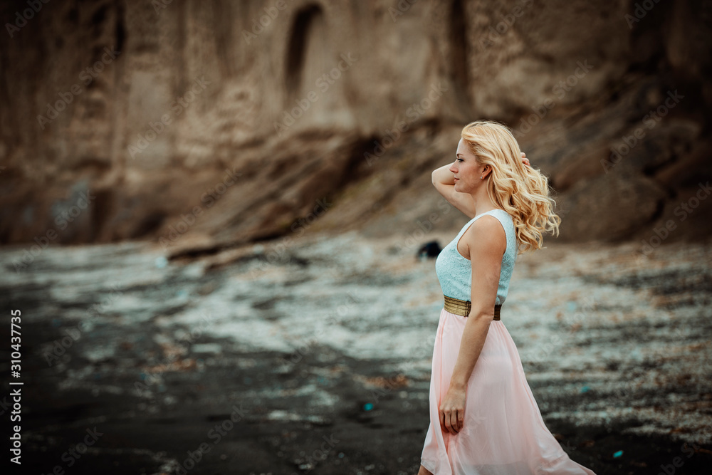 Wall mural blond woman on a black beach on Santorini, with cliff in the background