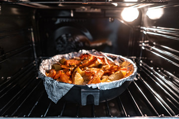 Baked potatoes with carrot and other spices in roasting pan.