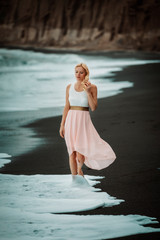 blond woman on a black beach on Santorini, with cliff in the background and a rough sea