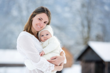 Beautiful mother in white dress and cute baby boy in knitted onesie