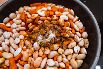 Carrots, garlic and beans with salt and spices in a pan before cooking.
