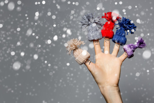 Funny christmas background with finger family in knitted hats with fallen snow over gray 