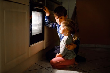 Little toddler girl and cute kid boy baking muffins and cookies in domestic kitchen. Two children,...