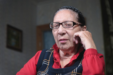 Portrait of an elderly pensive woman in glasses leaning on her arm indoors sitting and thinking. Elderly woman 80 years old