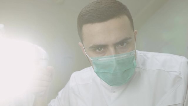 Low angle portrait of male dentist in surgical mask adjusting light