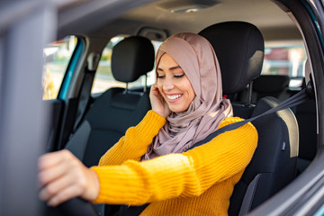 Beautiful woman with hijab driving a car. Portrait of a Middle Eastern woman driving a car, she is wearing a modern beige Abaya. Emirati woman driving a car.