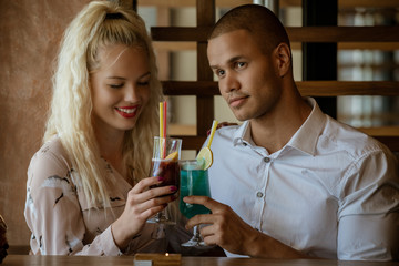 Young african man and blonde american woman drink cocktail, happy couple in bar drink cocktail and have fun