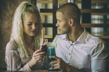 Young african man and blonde american woman drink cocktail, happy couple in bar drink cocktail and have fun