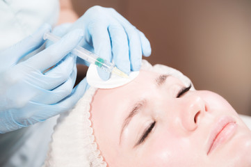 Obraz na płótnie Canvas Close-up Attractive young woman gets anti-aging face injections. She lies calmly in a clinic or salon. An experienced young cosmetologist fills female wrinkles with hyaluronic acid from a syringe