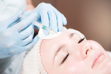Naklejka premium Close-up Attractive young woman gets anti-aging face injections. She lies calmly in a clinic or salon. An experienced young cosmetologist fills female wrinkles with hyaluronic acid from a syringe