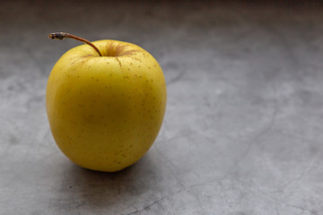 Side view of the yellow apple on the grey stone table