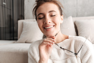 Image of woman with eyeglasses smiling while resting on sofa at home
