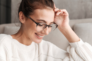 Image of young woman in eyeglasses smiling while resting on sofa at home