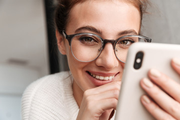 Image of woman in eyeglasses smiling and holding cellphone at home