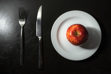 Red apples, knives and forks rest on white dish
