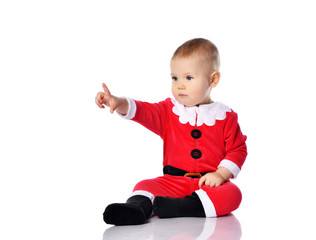 Little baby boy toddler in santa claus christmas costume is sitting pointing his finger forward isolated on white