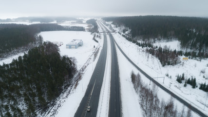 Freeway passing through the winter forest. The road goes away to the horizon line. Highway with cars .Aerial view.