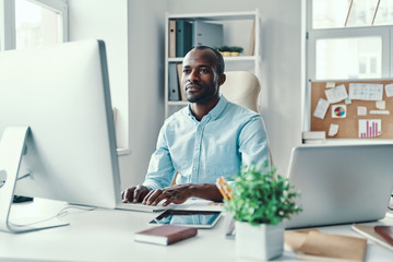 Concentrated young African man in shirt using computer while working in the office